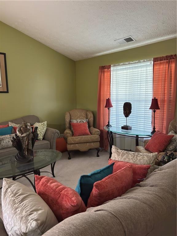 living area with vaulted ceiling, carpet, visible vents, and a textured ceiling