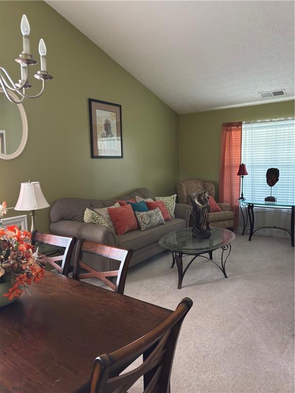 living room featuring visible vents, light carpet, a notable chandelier, and vaulted ceiling