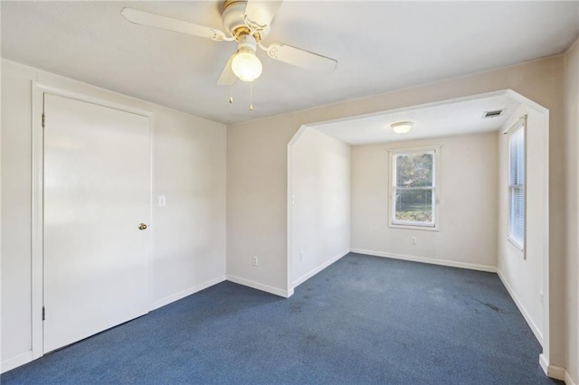 empty room with arched walkways, dark colored carpet, visible vents, a ceiling fan, and baseboards