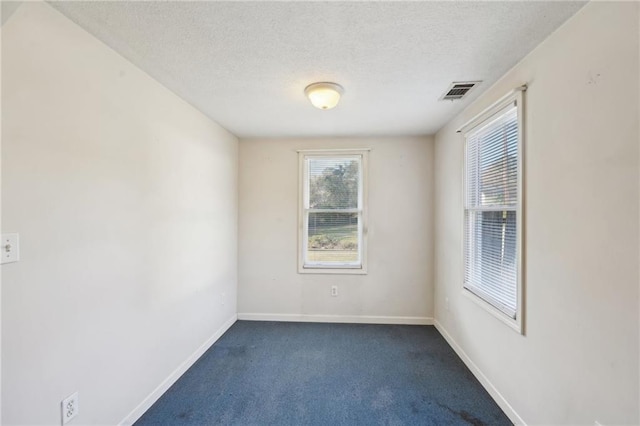 empty room with visible vents, dark carpet, a textured ceiling, and baseboards