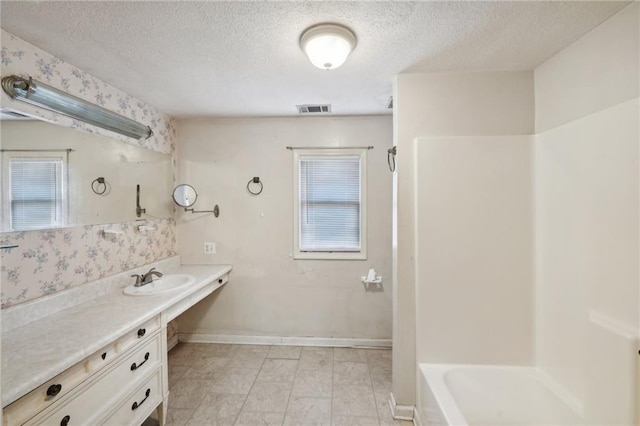 bathroom with a textured ceiling, vanity, visible vents, and baseboards