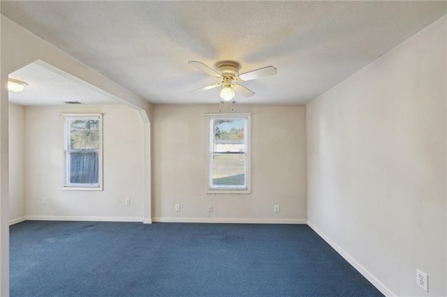 spare room featuring arched walkways, visible vents, baseboards, a ceiling fan, and dark colored carpet