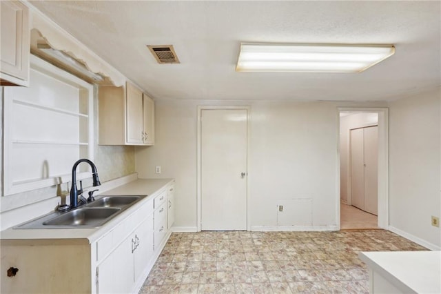 kitchen with light countertops, a sink, visible vents, and baseboards