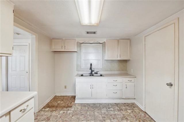 kitchen with light countertops, visible vents, a sink, and baseboards