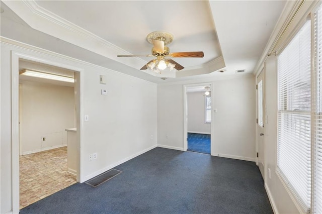 spare room with visible vents, a raised ceiling, dark colored carpet, and ornamental molding