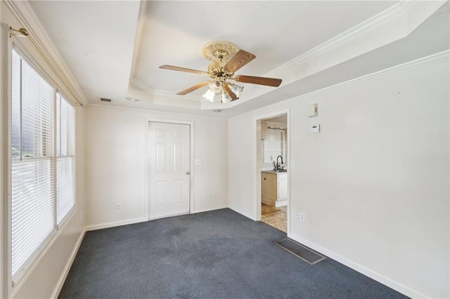 unfurnished bedroom with a sink, visible vents, a tray ceiling, dark carpet, and crown molding