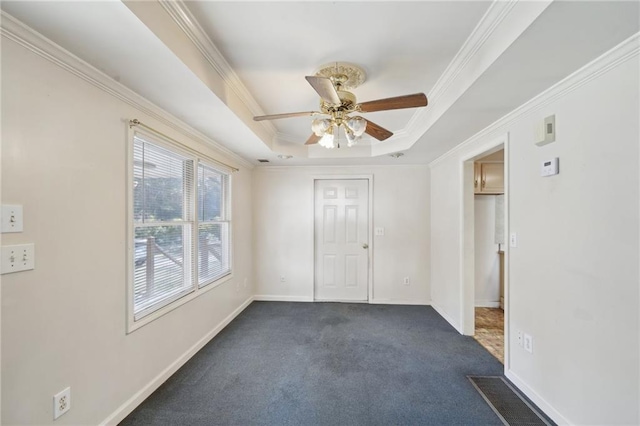 unfurnished room featuring baseboards, dark carpet, a raised ceiling, and crown molding