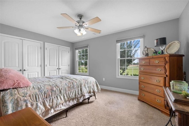 bedroom featuring ceiling fan, light colored carpet, and two closets