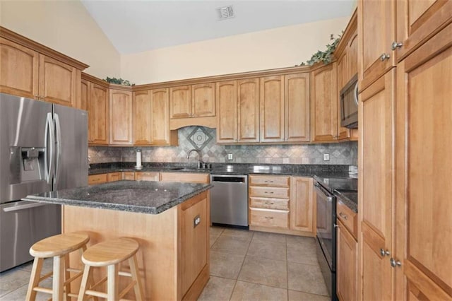 kitchen with a center island, light tile patterned floors, appliances with stainless steel finishes, tasteful backsplash, and a kitchen bar