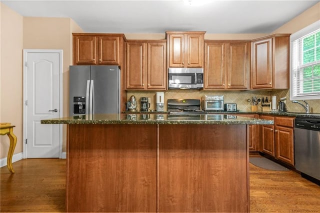 kitchen with dark stone counters, appliances with stainless steel finishes, a center island, and light wood-type flooring