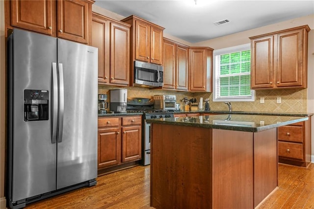 kitchen featuring light wood-style flooring, dark stone countertops, stainless steel appliances, tasteful backsplash, and a kitchen island