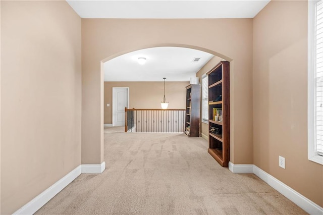 corridor with carpet floors, arched walkways, baseboards, and visible vents