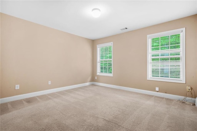 empty room with baseboards, visible vents, light colored carpet, and a wealth of natural light