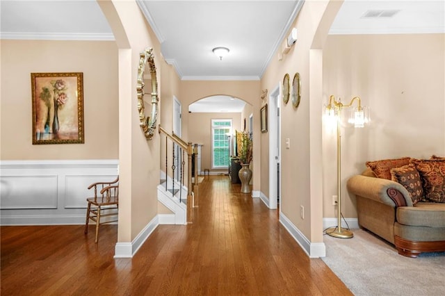 corridor featuring crown molding, arched walkways, wood finished floors, visible vents, and stairway