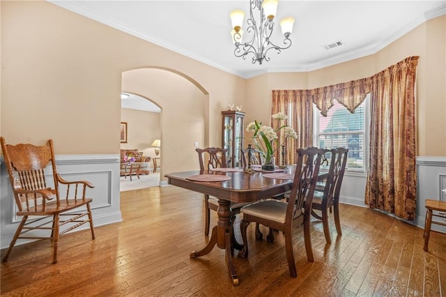 dining room with crown molding, arched walkways, hardwood / wood-style flooring, and visible vents