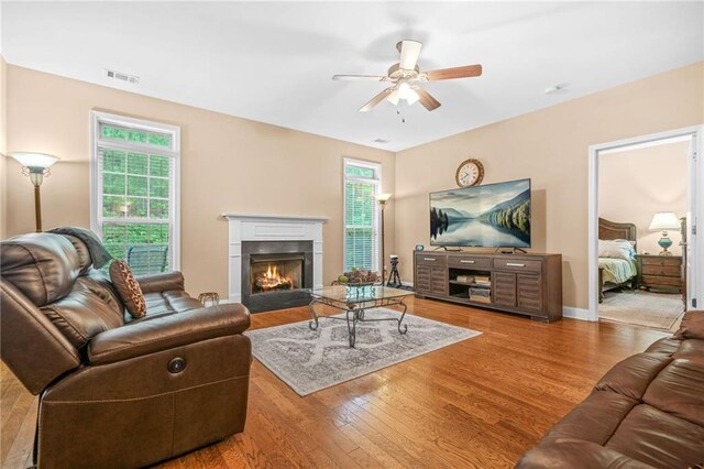 living area featuring ceiling fan, a fireplace, baseboards, wood finished floors, and visible vents