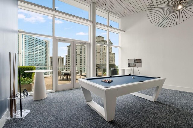 recreation room with a wall of windows, a view of city, billiards, a towering ceiling, and carpet