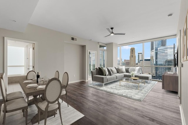 living area with expansive windows, visible vents, a view of city, ceiling fan, and wood finished floors