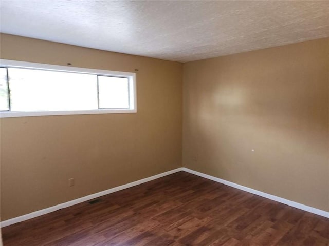 empty room with dark hardwood / wood-style flooring and a textured ceiling