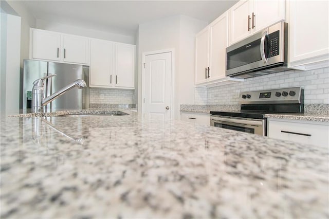 409 Glenn Trl, Winder, GA 30680 - kitchen featuring stainless steel appliances, decorative backsplash, white cabinetry, and light stone counters