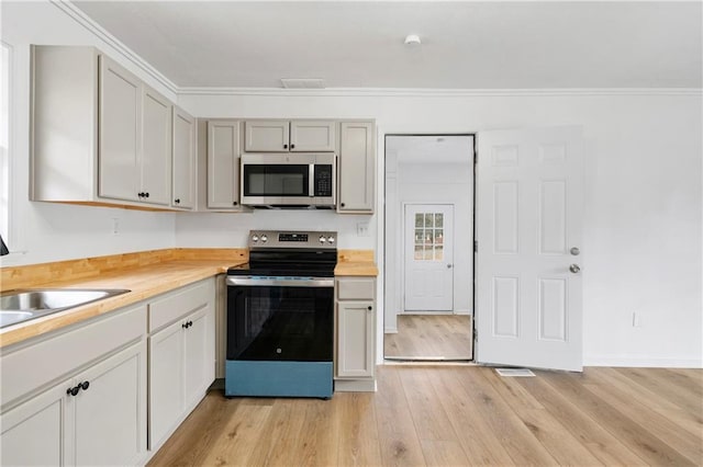 kitchen with sink, butcher block countertops, crown molding, light hardwood / wood-style flooring, and appliances with stainless steel finishes