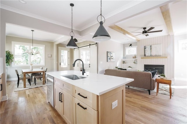 kitchen featuring dishwasher, hanging light fixtures, sink, light wood-type flooring, and a kitchen island with sink