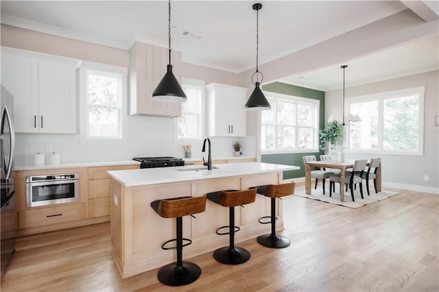 kitchen with white cabinets, light wood-type flooring, sink, an island with sink, and stainless steel appliances