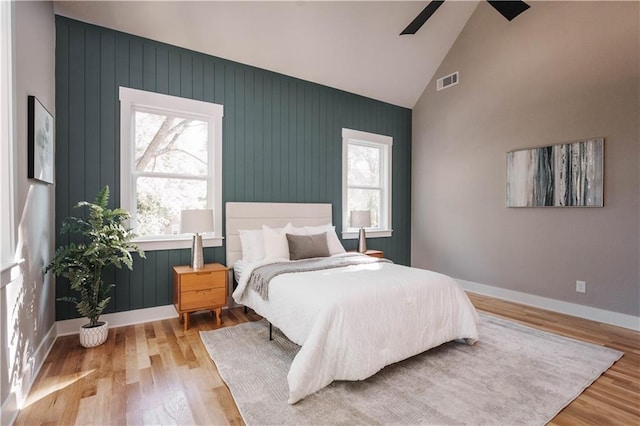 bedroom featuring ceiling fan, high vaulted ceiling, light hardwood / wood-style flooring, and multiple windows