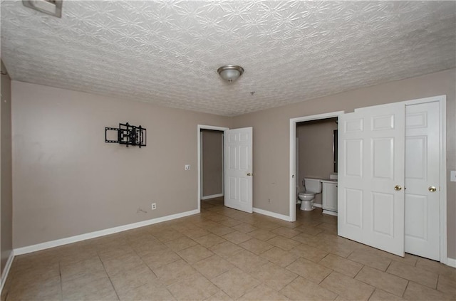unfurnished bedroom featuring light tile patterned floors, baseboards, and ensuite bath