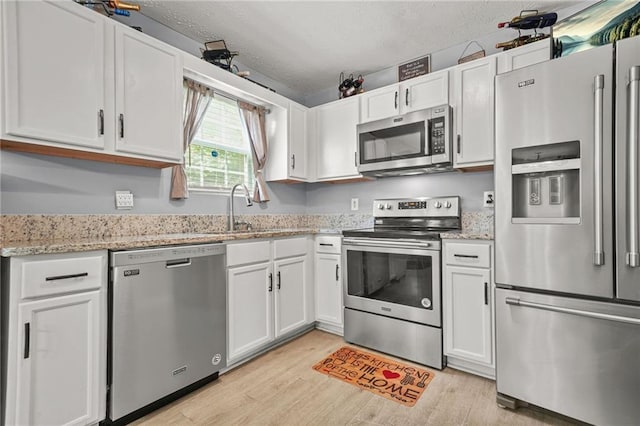 30 Creek Bottom Dr, Covington, GA 30014 - kitchen featuring stainless steel appliances, light wood finished floors, white cabinets, a textured ceiling, and light stone countertops