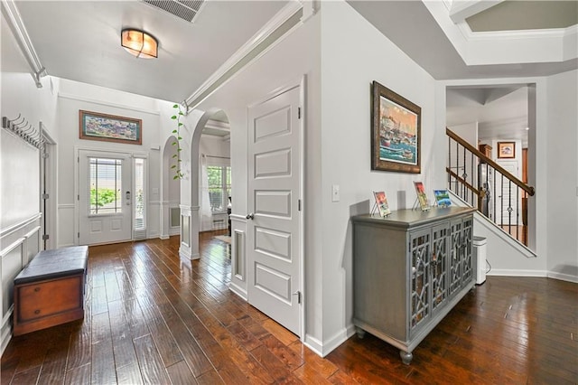 entryway with dark wood-type flooring, visible vents, arched walkways, and crown molding