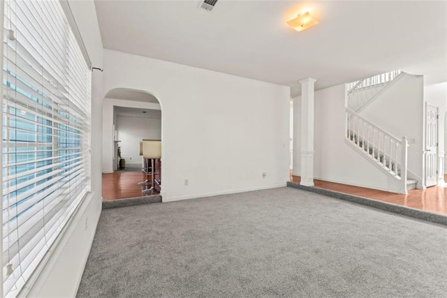 unfurnished living room featuring arched walkways, baseboards, visible vents, stairway, and carpet floors