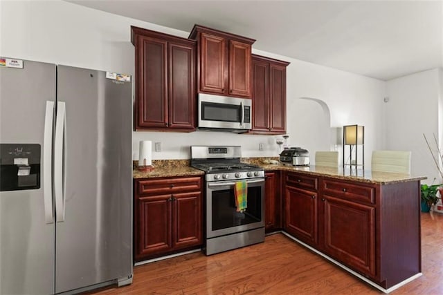 kitchen with dark brown cabinets, a peninsula, wood finished floors, and appliances with stainless steel finishes