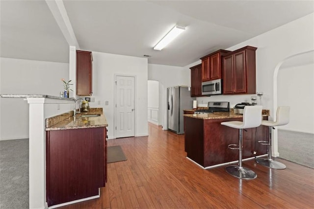 kitchen with a sink, reddish brown cabinets, stone countertops, stainless steel appliances, and a peninsula