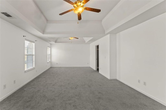 unfurnished room featuring a tray ceiling, baseboards, visible vents, carpet, and a ceiling fan