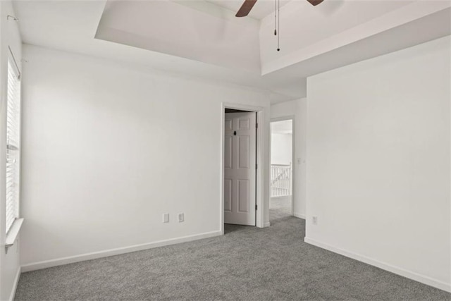 carpeted spare room featuring a raised ceiling, a ceiling fan, and baseboards