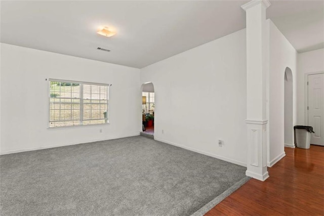empty room with carpet flooring, arched walkways, baseboards, visible vents, and wood finished floors