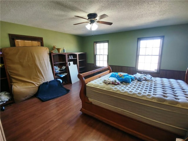 bedroom featuring ceiling fan, dark wood-type flooring, wooden walls, and a textured ceiling