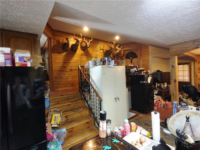 kitchen with black fridge, wooden walls, and a textured ceiling