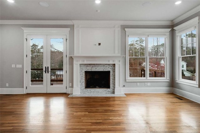 unfurnished living room featuring crown molding, wood-type flooring, a tile fireplace, and french doors