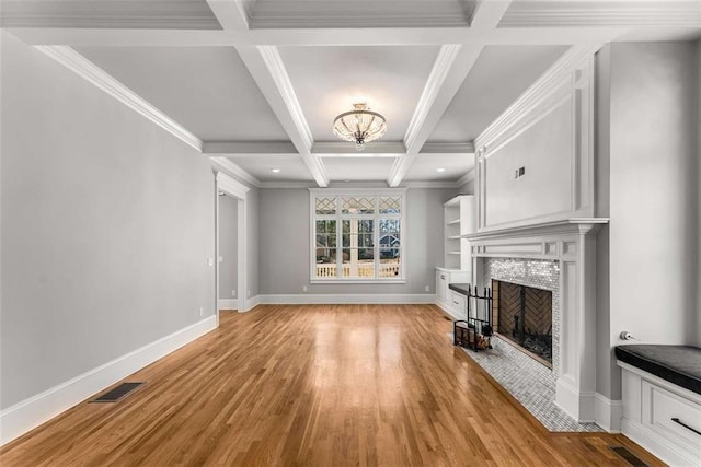 unfurnished living room featuring coffered ceiling, ornamental molding, a tiled fireplace, beamed ceiling, and light wood-type flooring