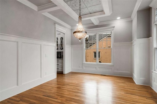 unfurnished dining area with an inviting chandelier, ornamental molding, coffered ceiling, and wood-type flooring