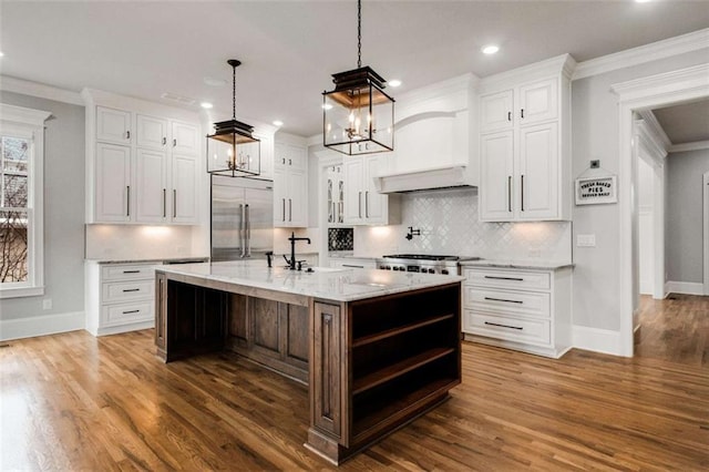 kitchen with white cabinets, stainless steel built in fridge, and a center island with sink