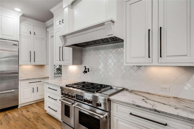 kitchen featuring white cabinetry, light stone counters, light wood-type flooring, high quality appliances, and backsplash