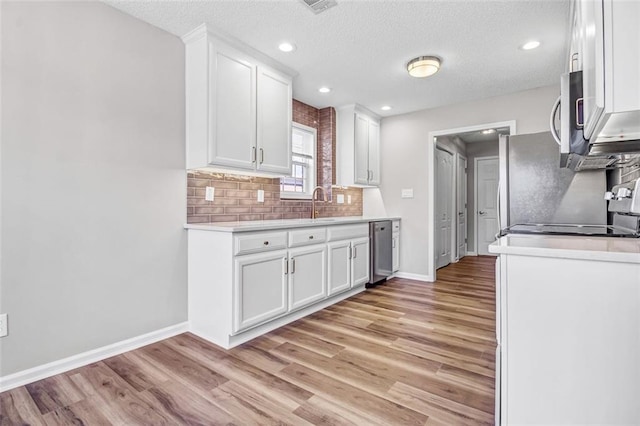 kitchen with a textured ceiling, light wood-type flooring, appliances with stainless steel finishes, decorative backsplash, and white cabinets