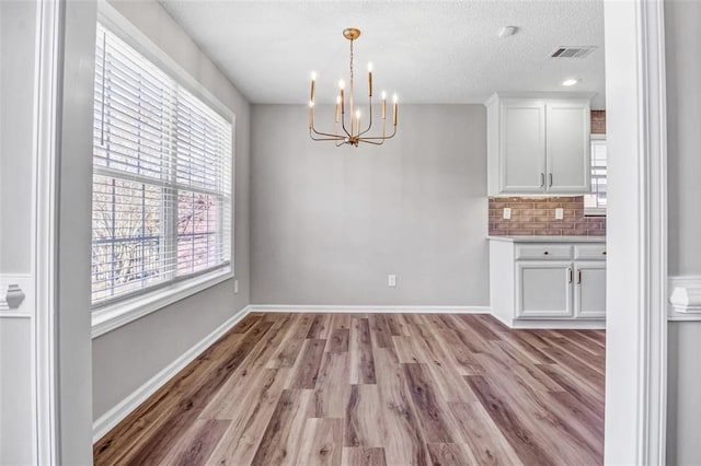 unfurnished dining area featuring a notable chandelier, light hardwood / wood-style flooring, and a textured ceiling