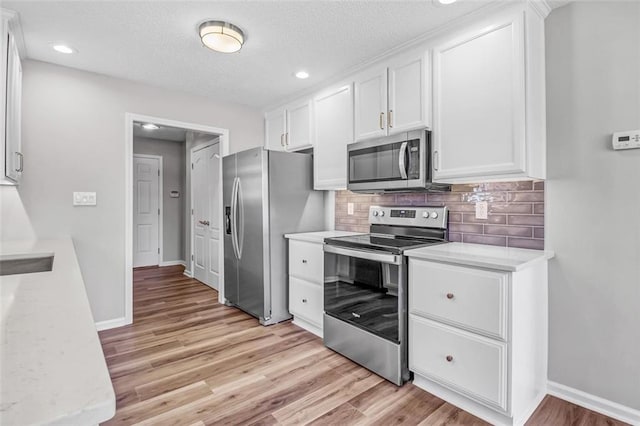 kitchen with a textured ceiling, appliances with stainless steel finishes, light hardwood / wood-style floors, decorative backsplash, and white cabinets