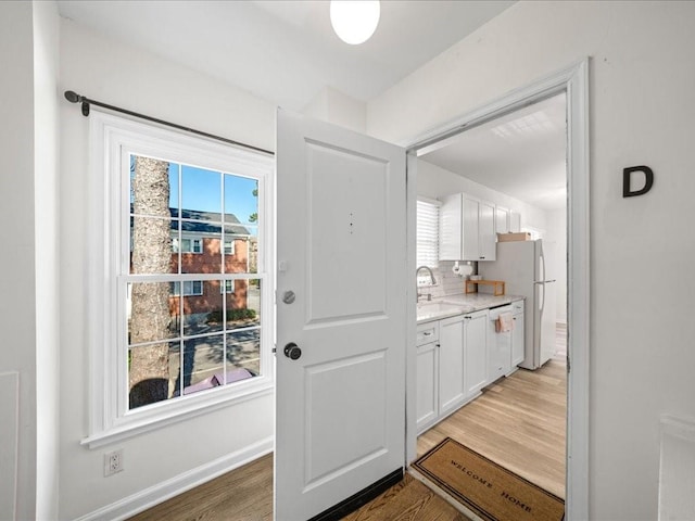 doorway to outside featuring baseboards, a sink, and light wood finished floors