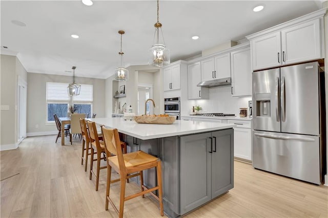 kitchen featuring decorative light fixtures, a breakfast bar area, white cabinets, a kitchen island with sink, and stainless steel appliances