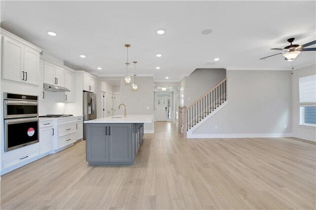 kitchen featuring pendant lighting, a breakfast bar area, white cabinets, stainless steel appliances, and a center island with sink